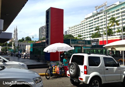 Congested city corner with a son-cone vender, metro station, cars, buildings