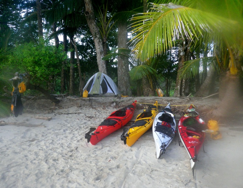 4 kayaks beached on white sand in front of tent in the woods
