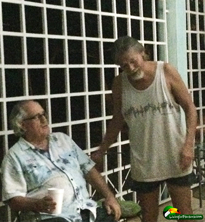 2 middle aged men, one sitting and one standing, chatting.
