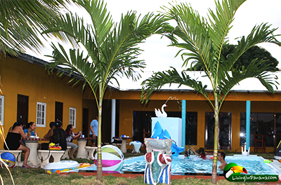 swimming pool surrounded by people, palm trees, fountain, and hotel rooms