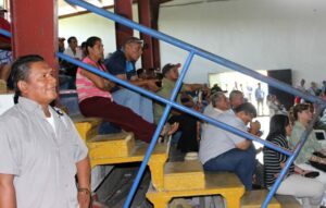 Crowd of people sitting inside on bleachers listening to speeches