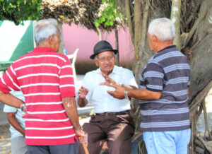 1 man wearing a fedora and 2 men facing him - all chatting