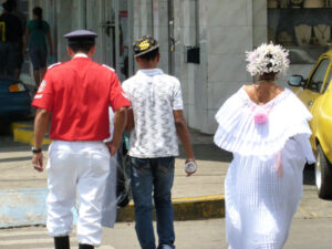 3 people walking away: military man, young man with baseball hate, and young woman in traditional Panamanian costume