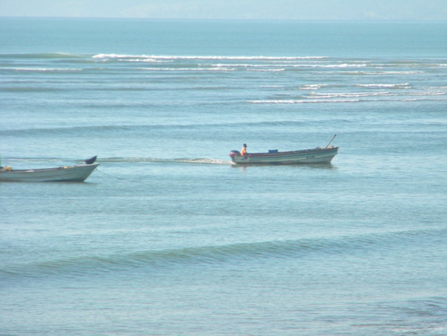 calm ocean with 2 fishing boats going by close to shore